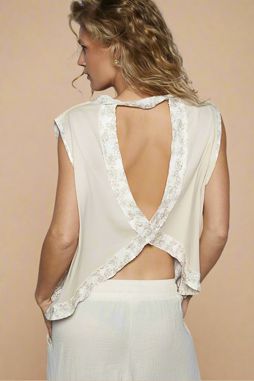 Woman wearing a beige sleeveless top with lace details and a open back on a plain background