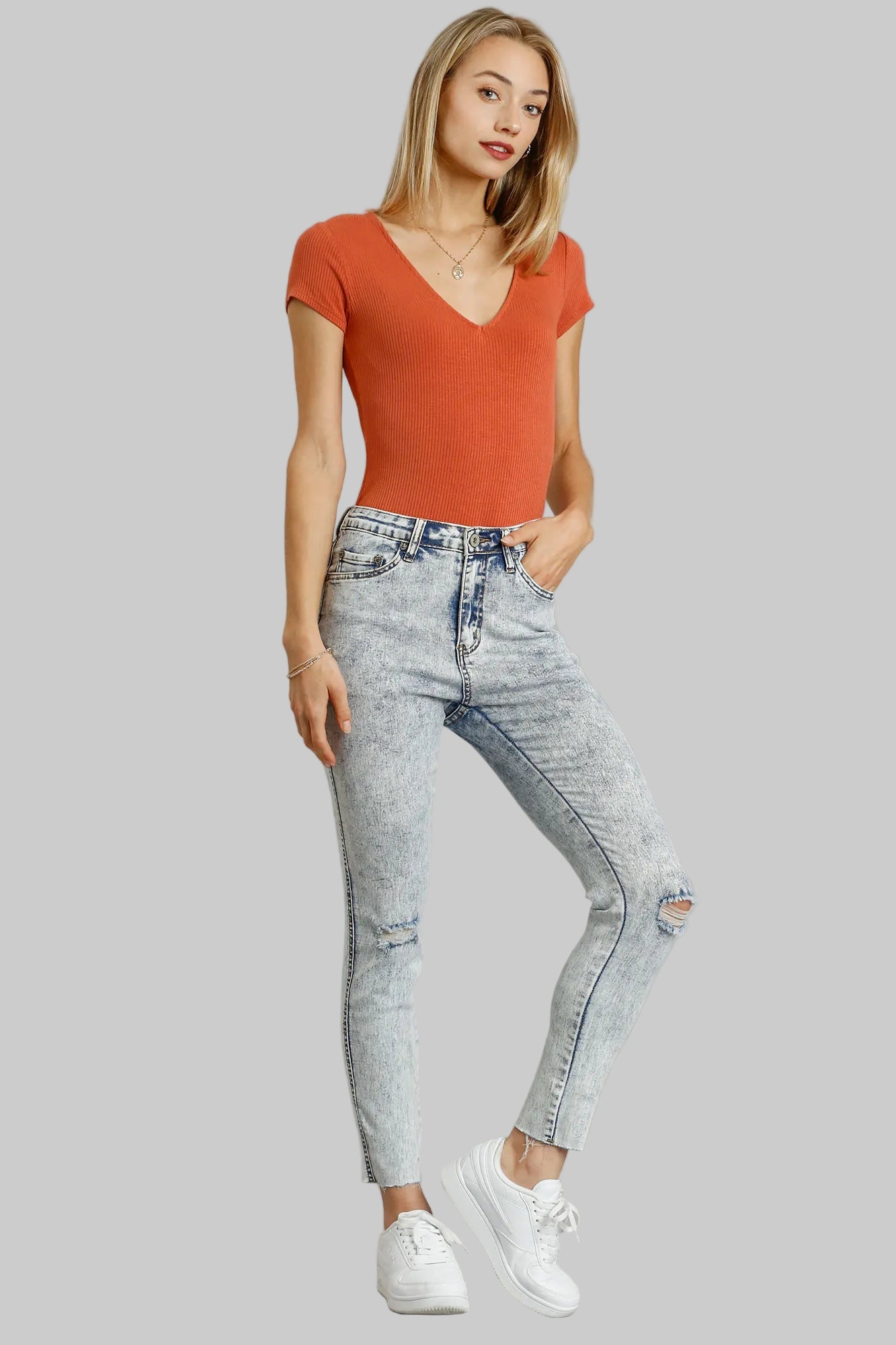 Woman wearing a red top and light blue jeans on a gray background