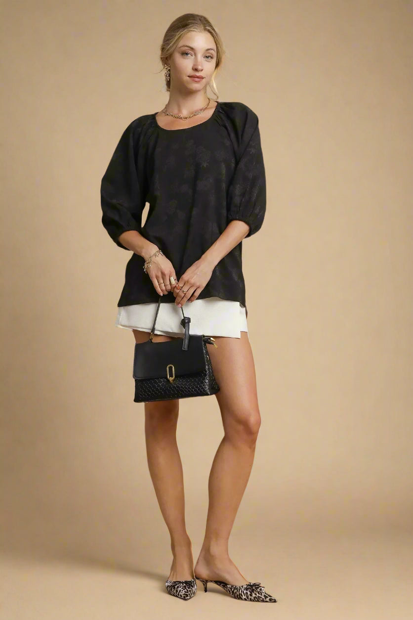 Woman wearing a black top and white shorts with a black handbag on a beige background