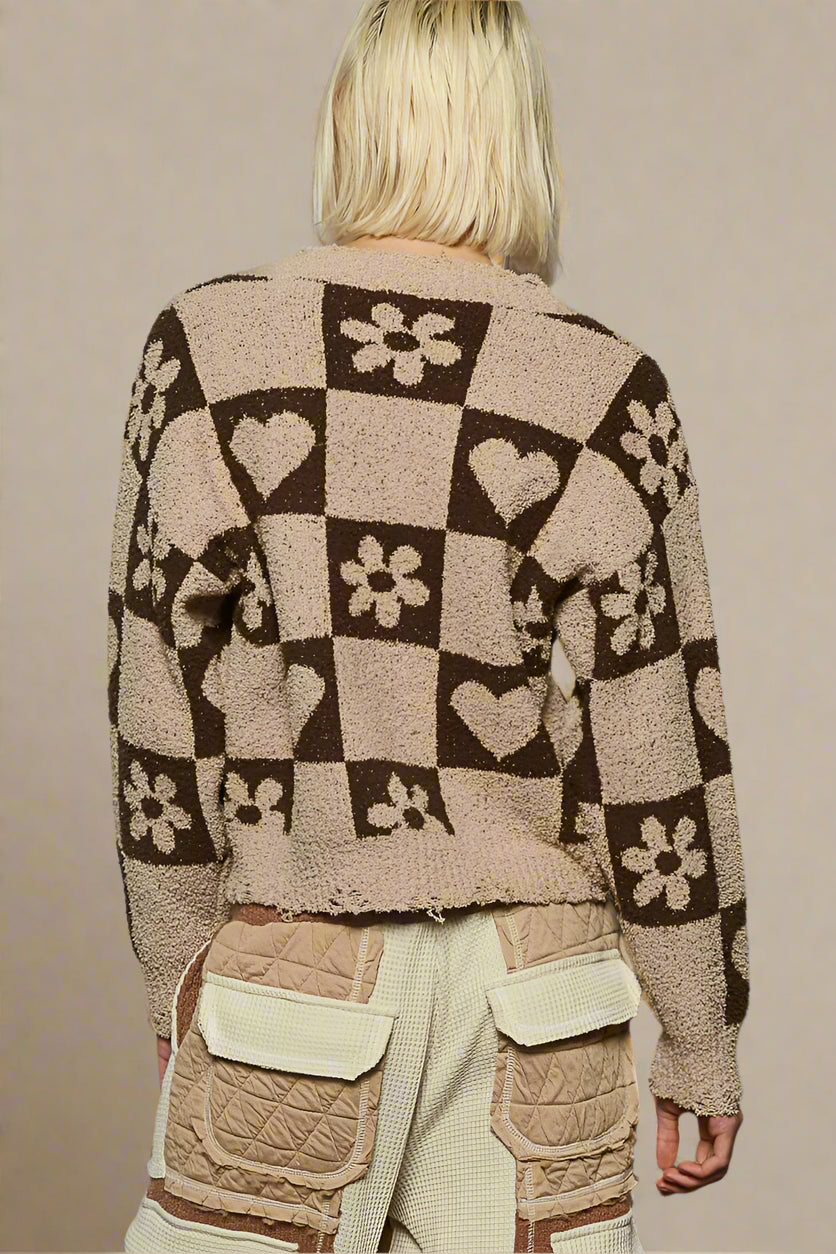 Person wearing a patterned cardigan with flowers and hearts on a plain background