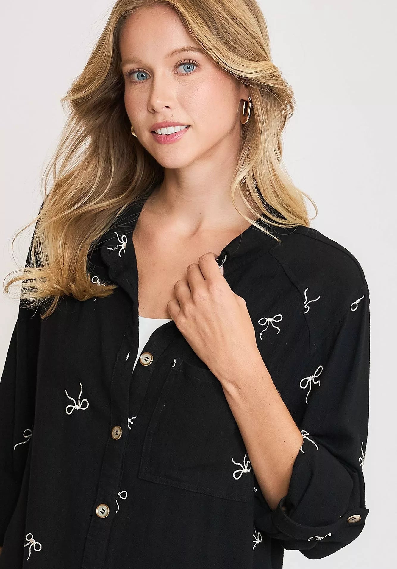 Woman wearing a black jacket with white bow patterns on a plain background