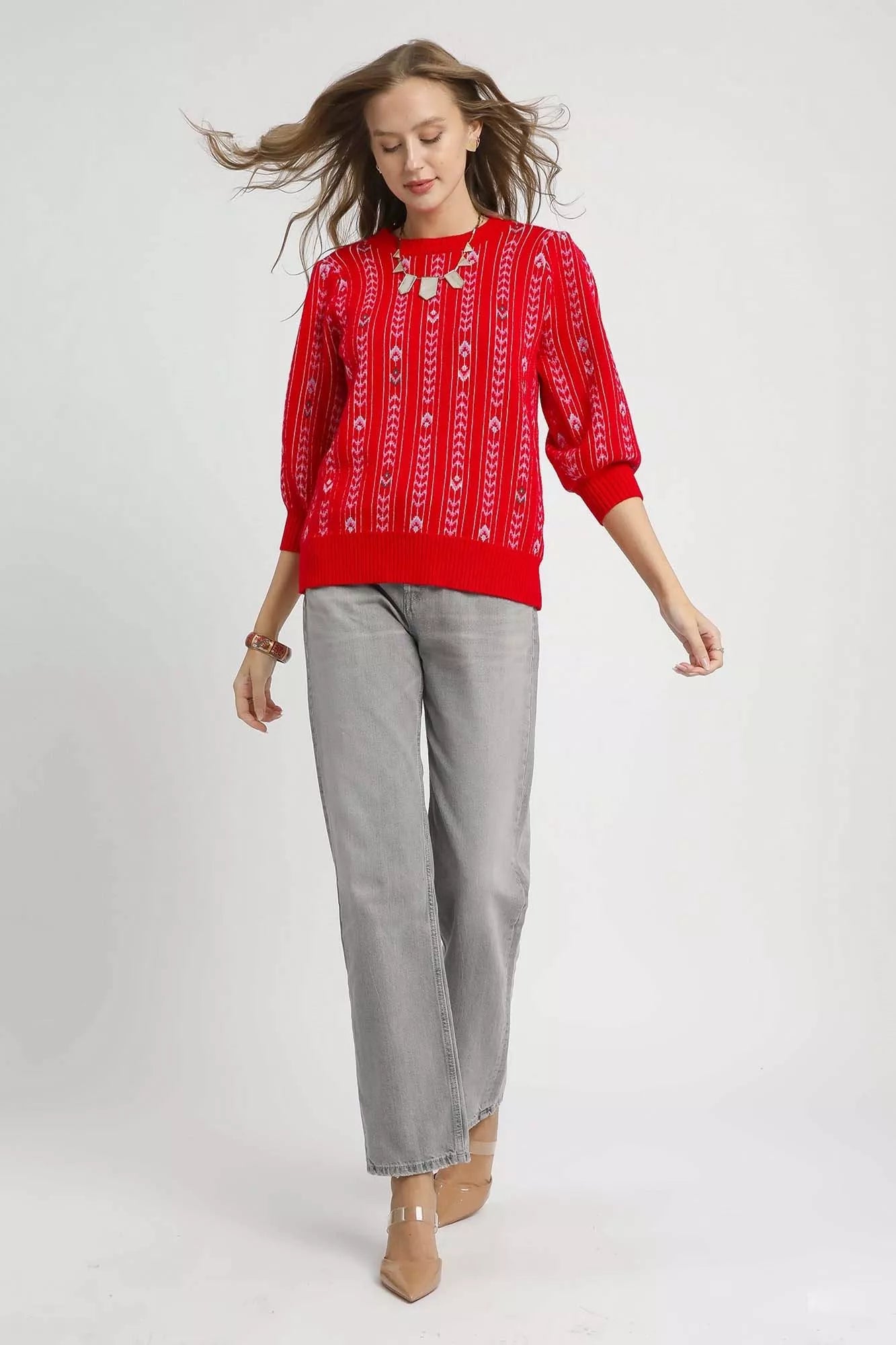 Woman wearing a red patterned top and gray pants on a white background