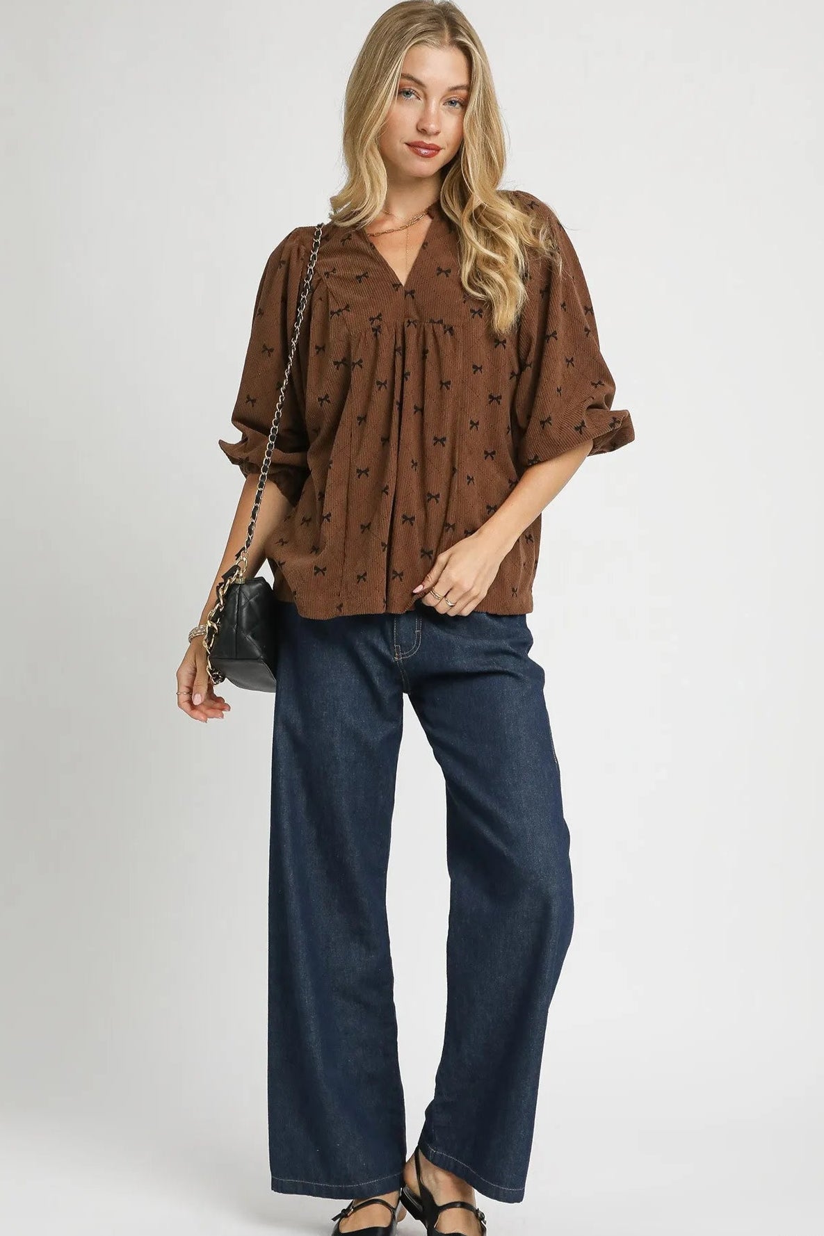 Woman wearing a brown patterned blouse and blue jeans on a white background