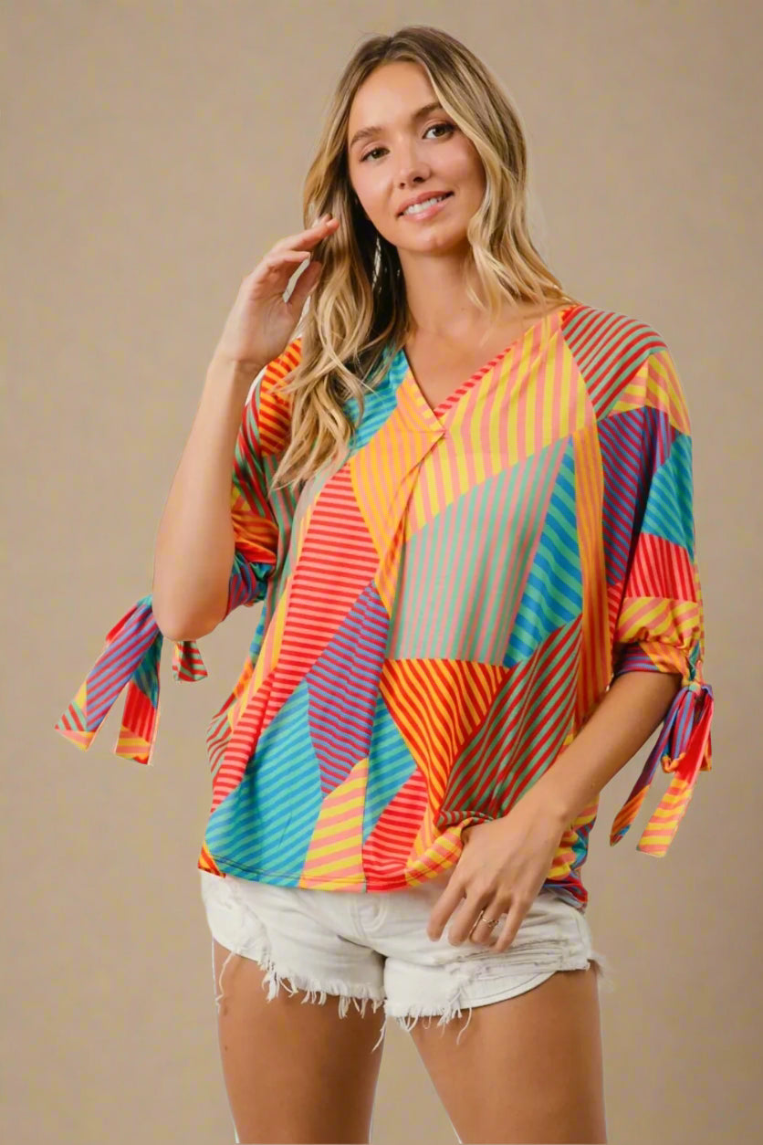 Woman wearing a colorful striped shirt with tassels in front of a beige background