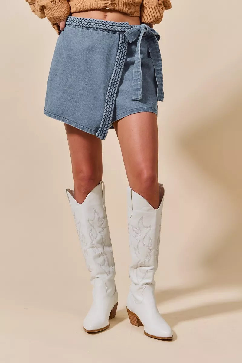 Person wearing a denim wrap skirt and white knee-high boots on a beige background