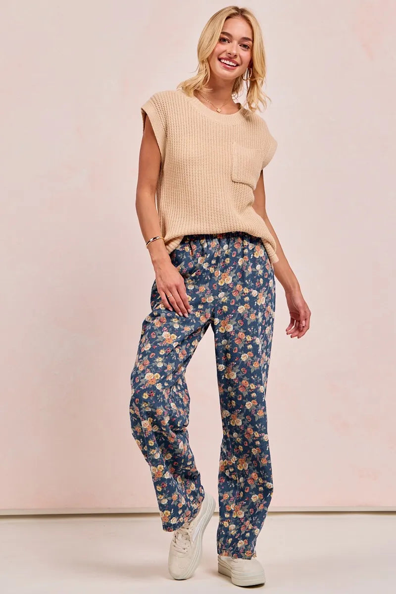 Woman wearing a beige sleeveless top and blue floral pants on a pink background