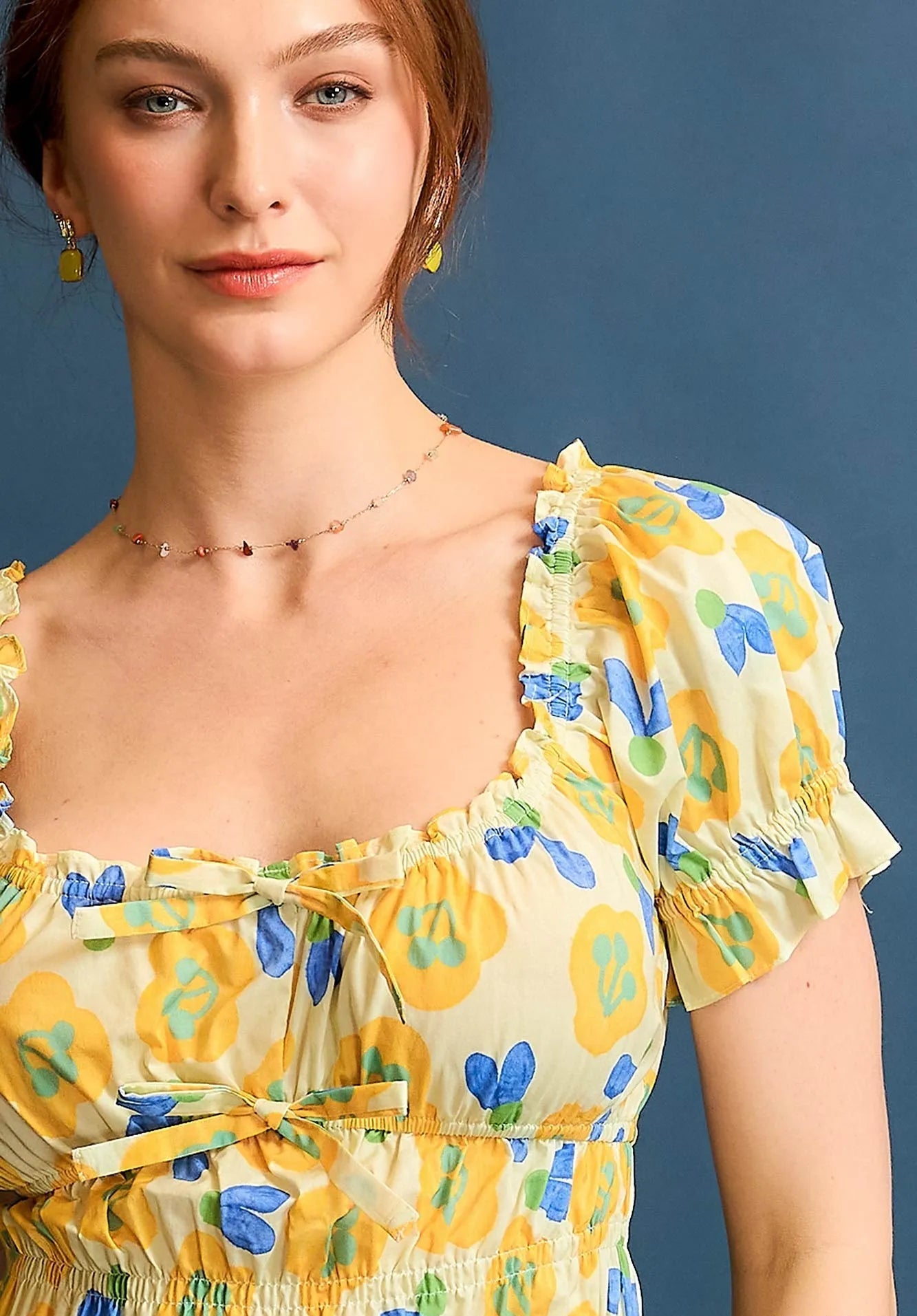Woman wearing a yellow floral dress against a blue background