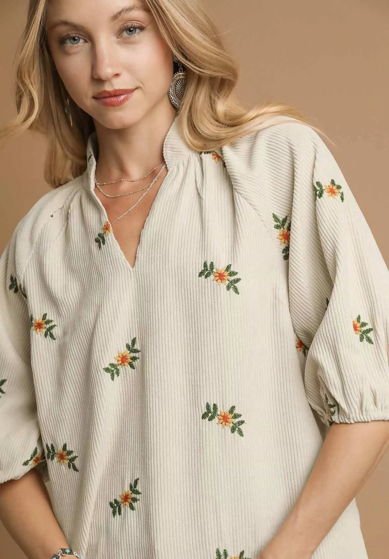 Woman wearing a cream-colored blouse with floral embroidery on a beige background