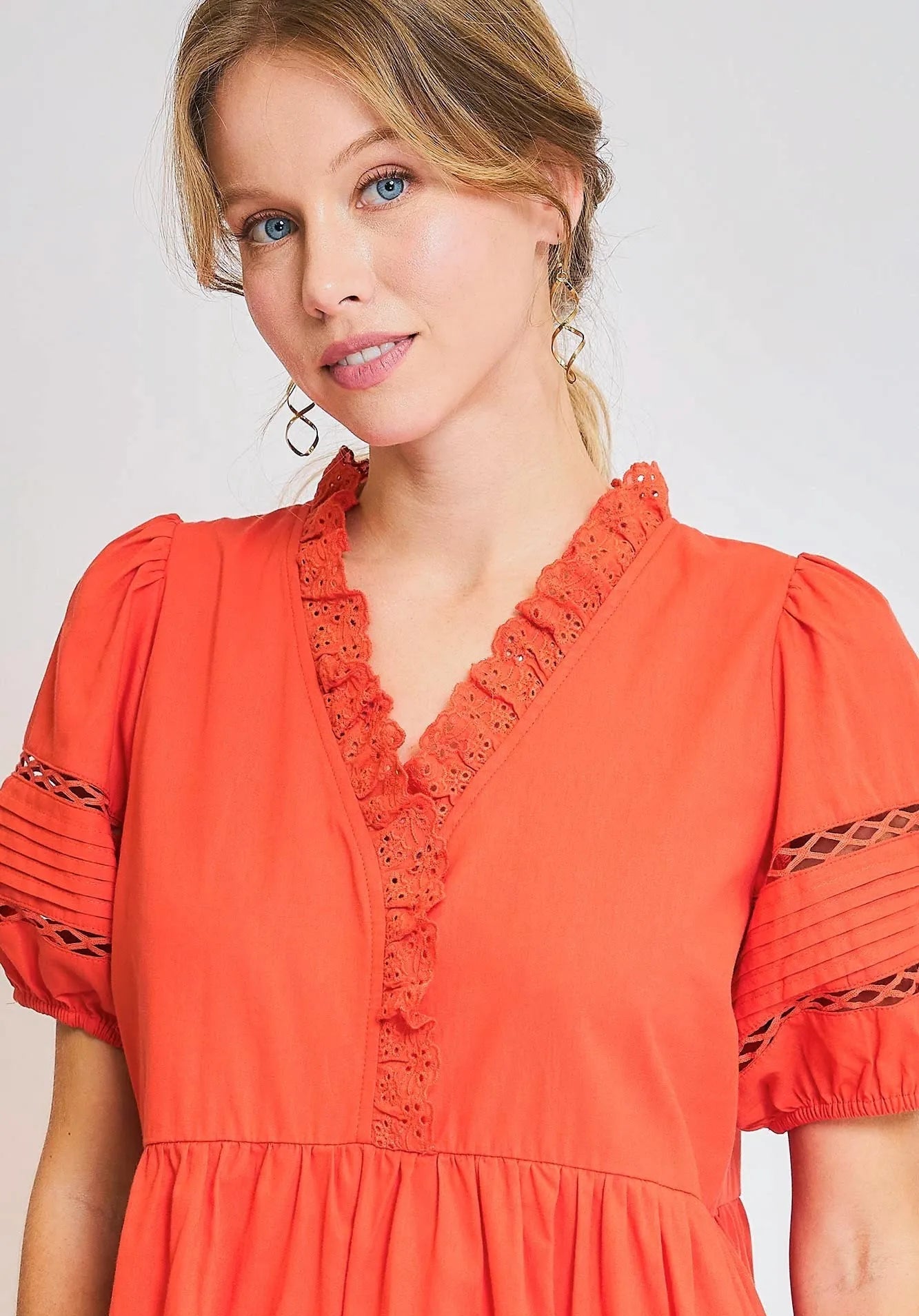 Woman wearing a tomato red dress with lace details on a white background