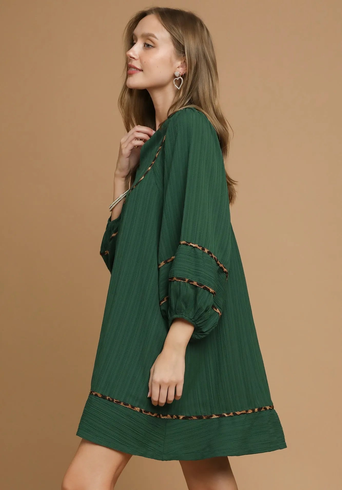 Woman wearing a green dress with brown trim on a beige background