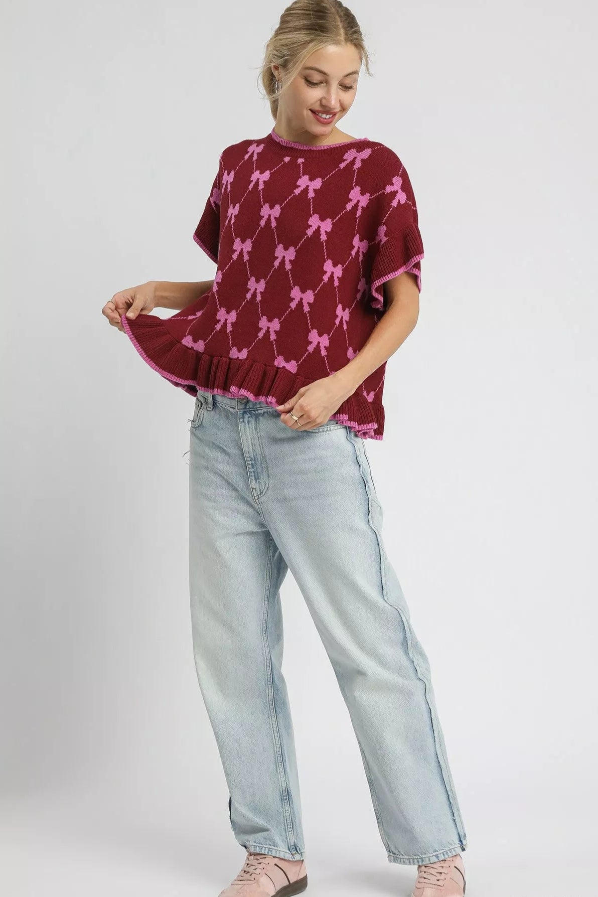 Woman wearing a burgundy sweater with pink dog pattern and light blue jeans on a white background