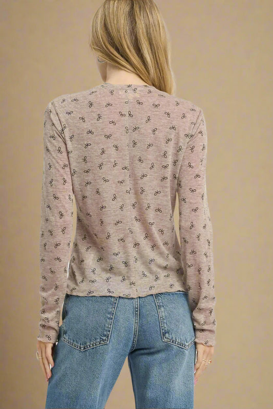 Person wearing a taupe long-sleeve top with a subtle pattern and blue jeans on a beige background.