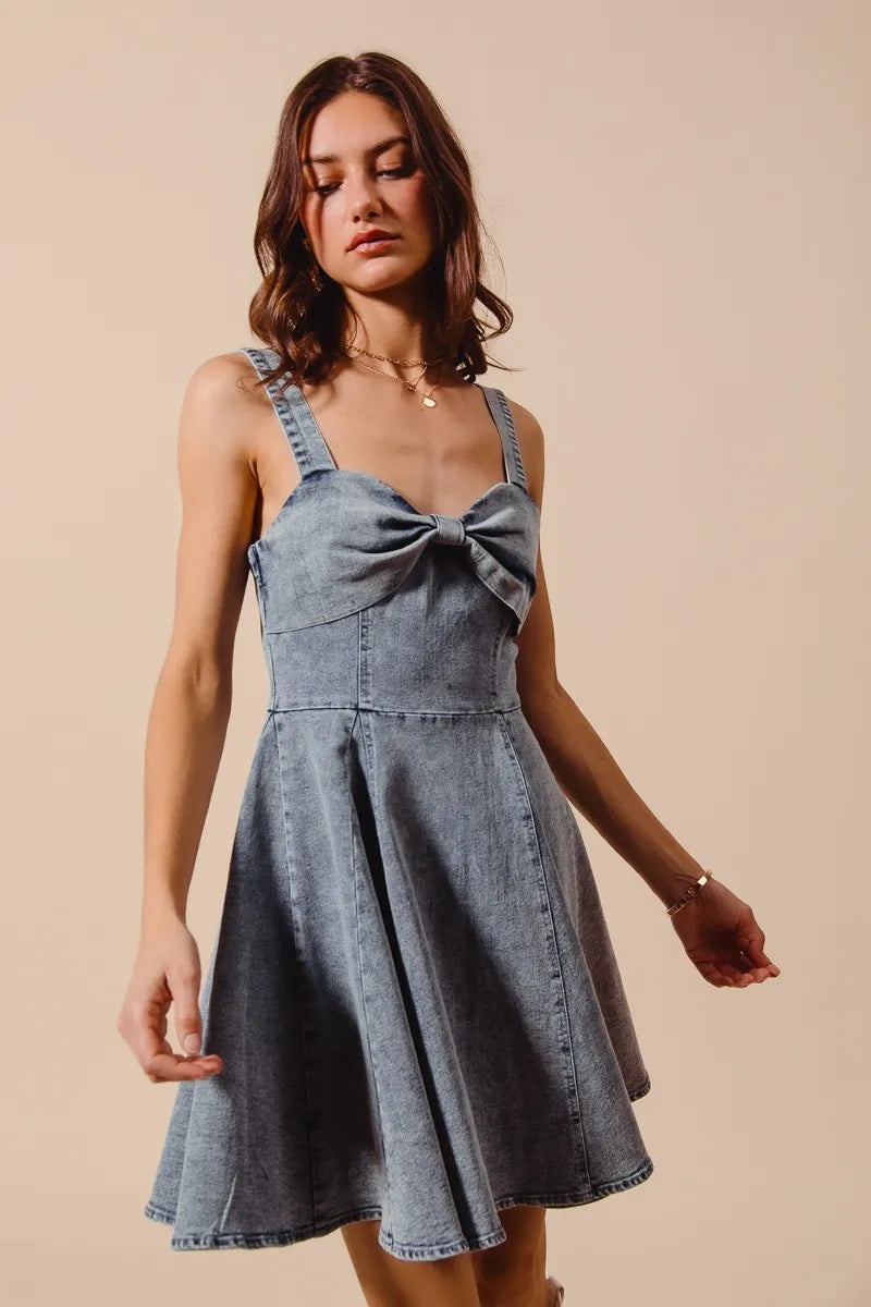 Woman wearing a denim dress with a bow detail on a beige background