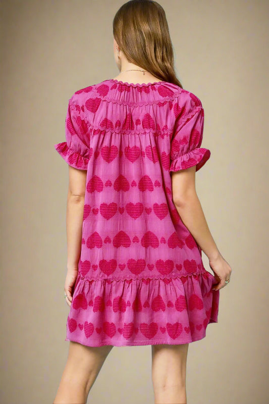 Woman wearing a pink dress with red heart patterns against a beige background