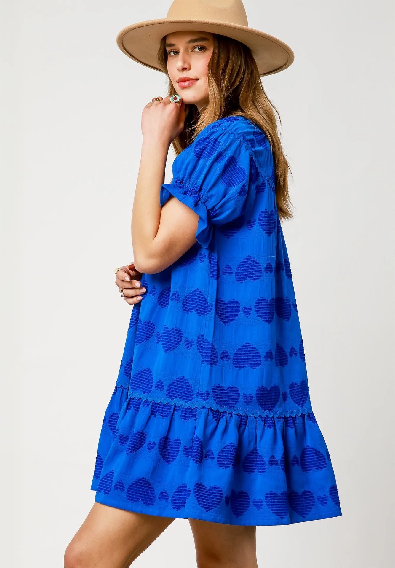 Woman wearing a blue dress with a pattern and a beige hat on a white background