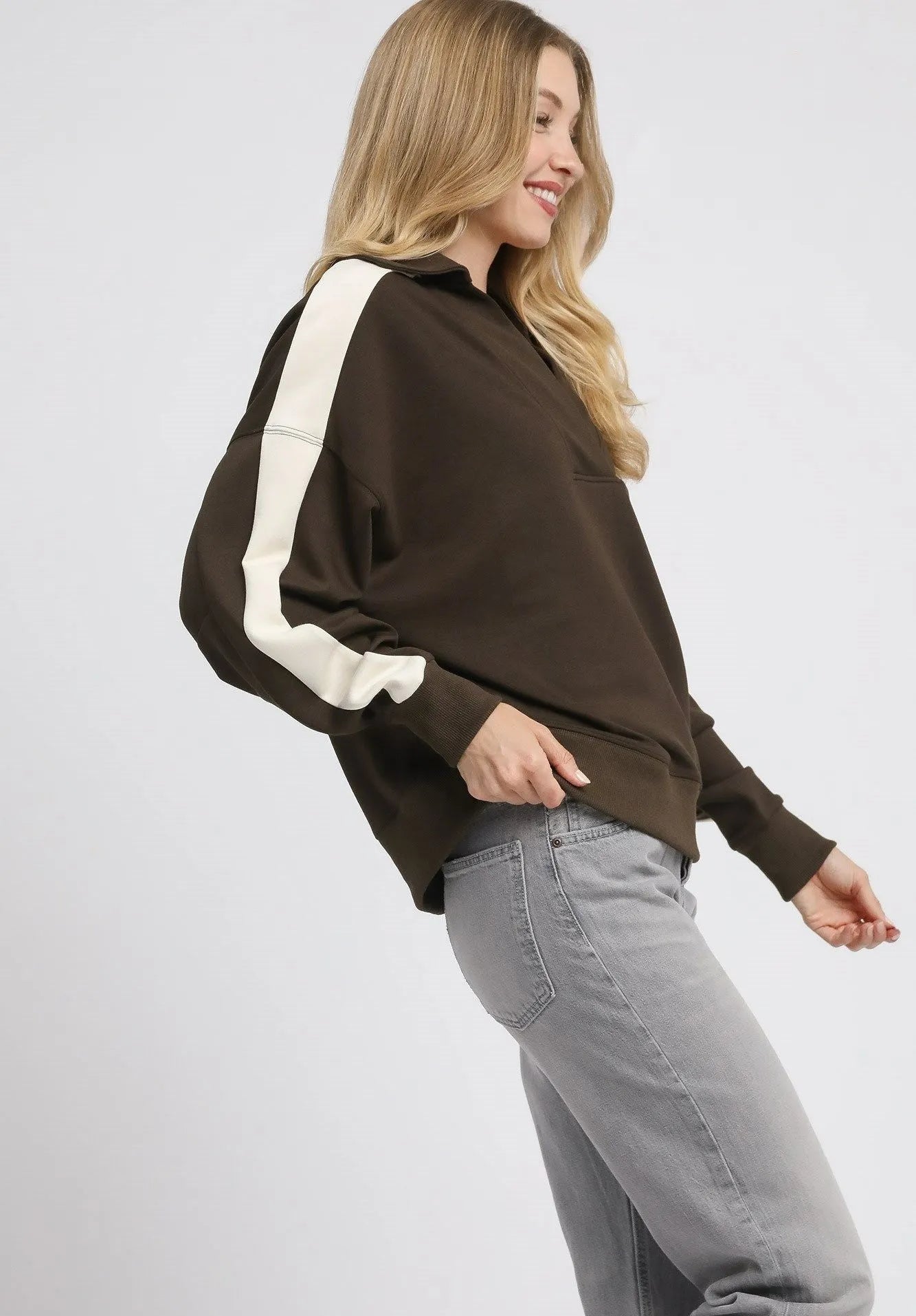 Woman wearing a brown sweater with white stripes and gray jeans on a light gray background