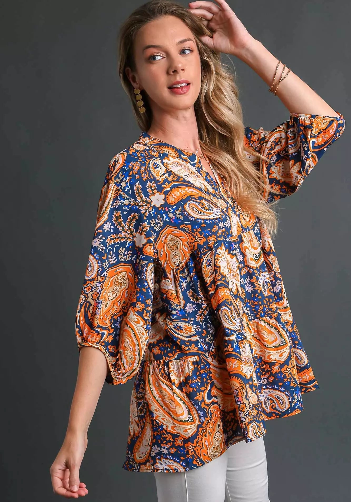 Woman wearing a patterned teal, orange, and blue blouse against a dark background