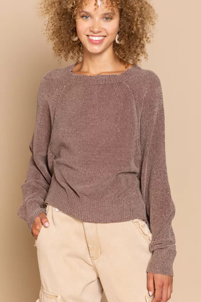 Woman wearing a brown sweater and beige pants against a beige background
