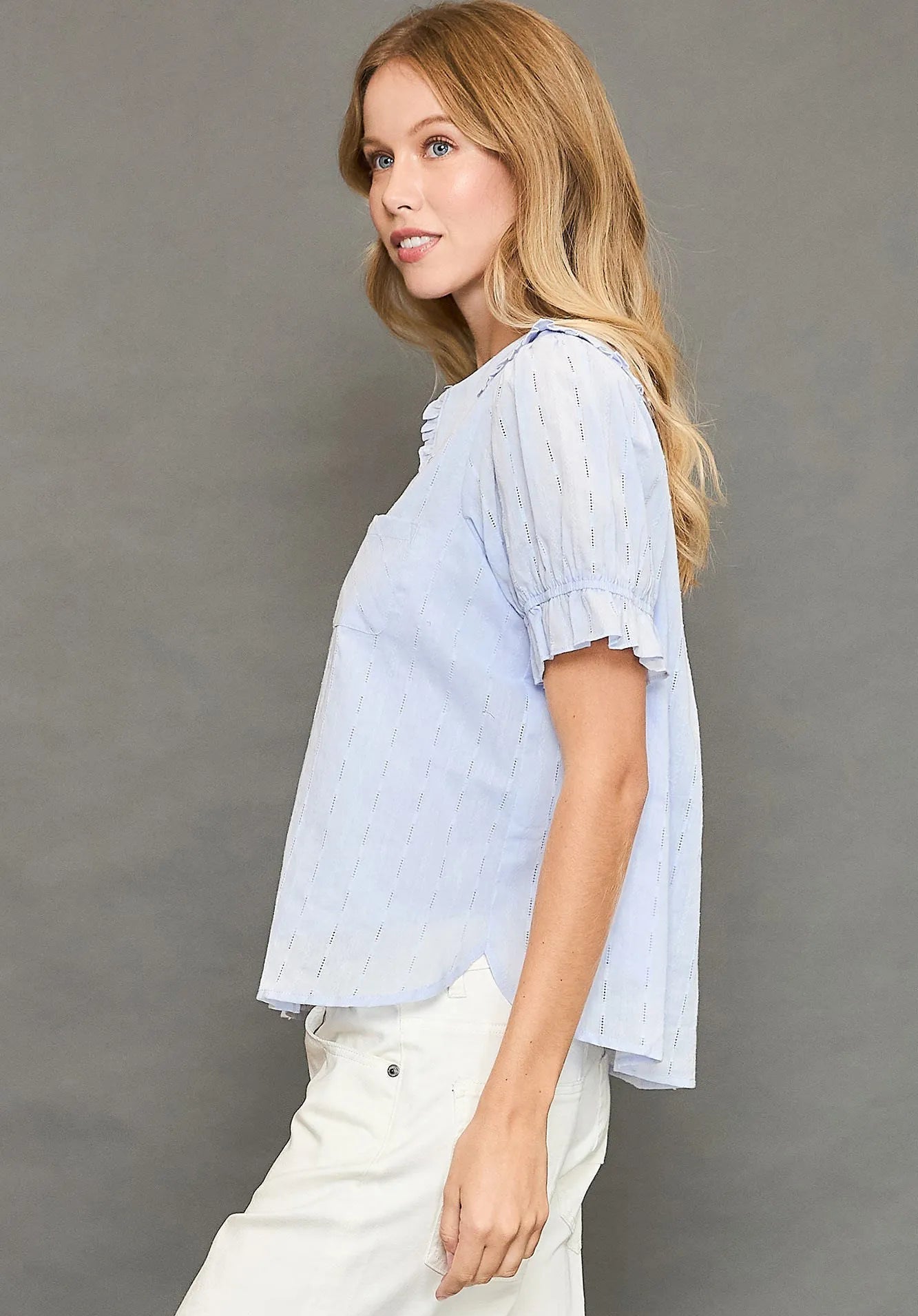 Woman wearing a light blue striped shirt and white pants against a gray background