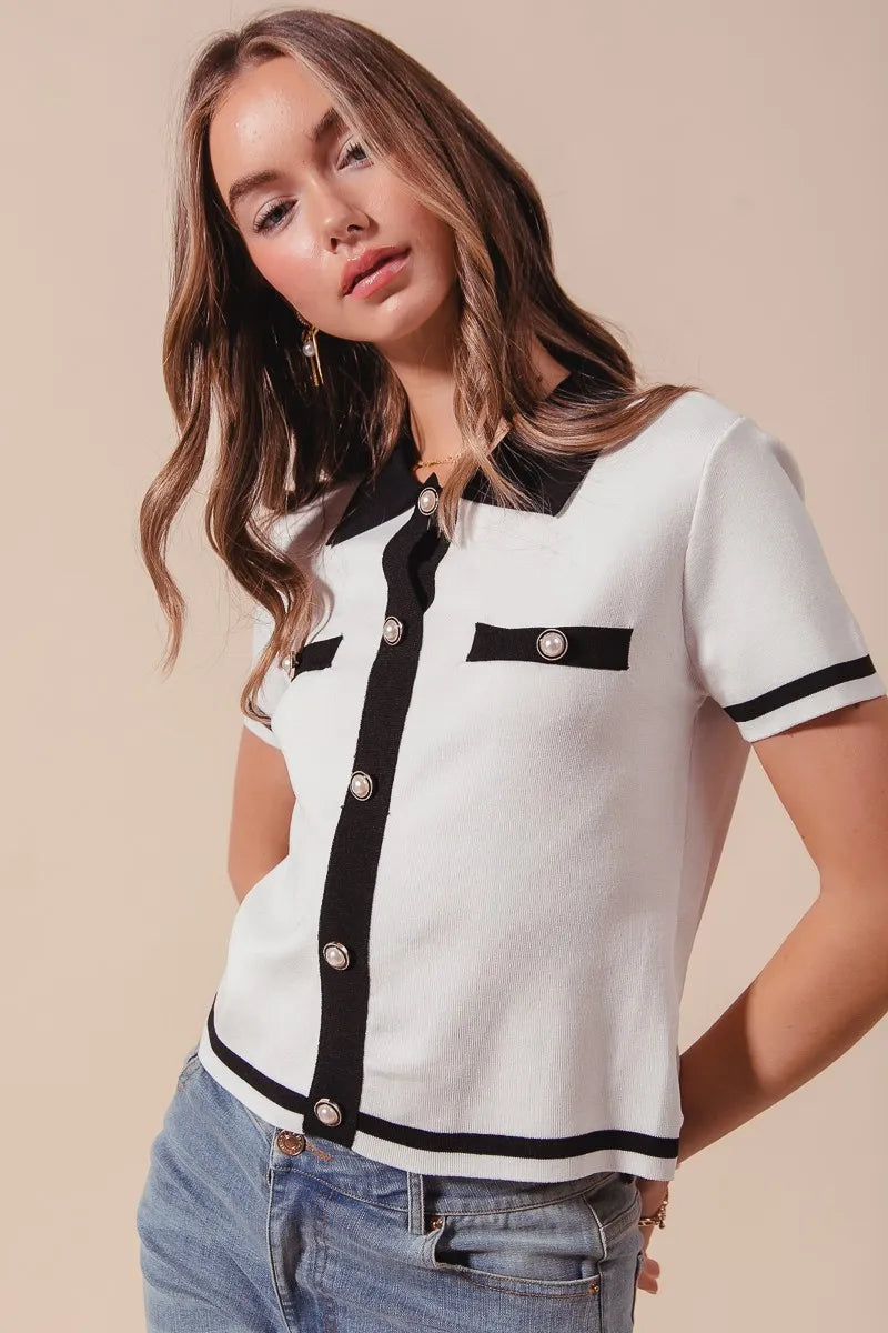 Woman wearing a white blouse with black accents and blue jeans on a beige background