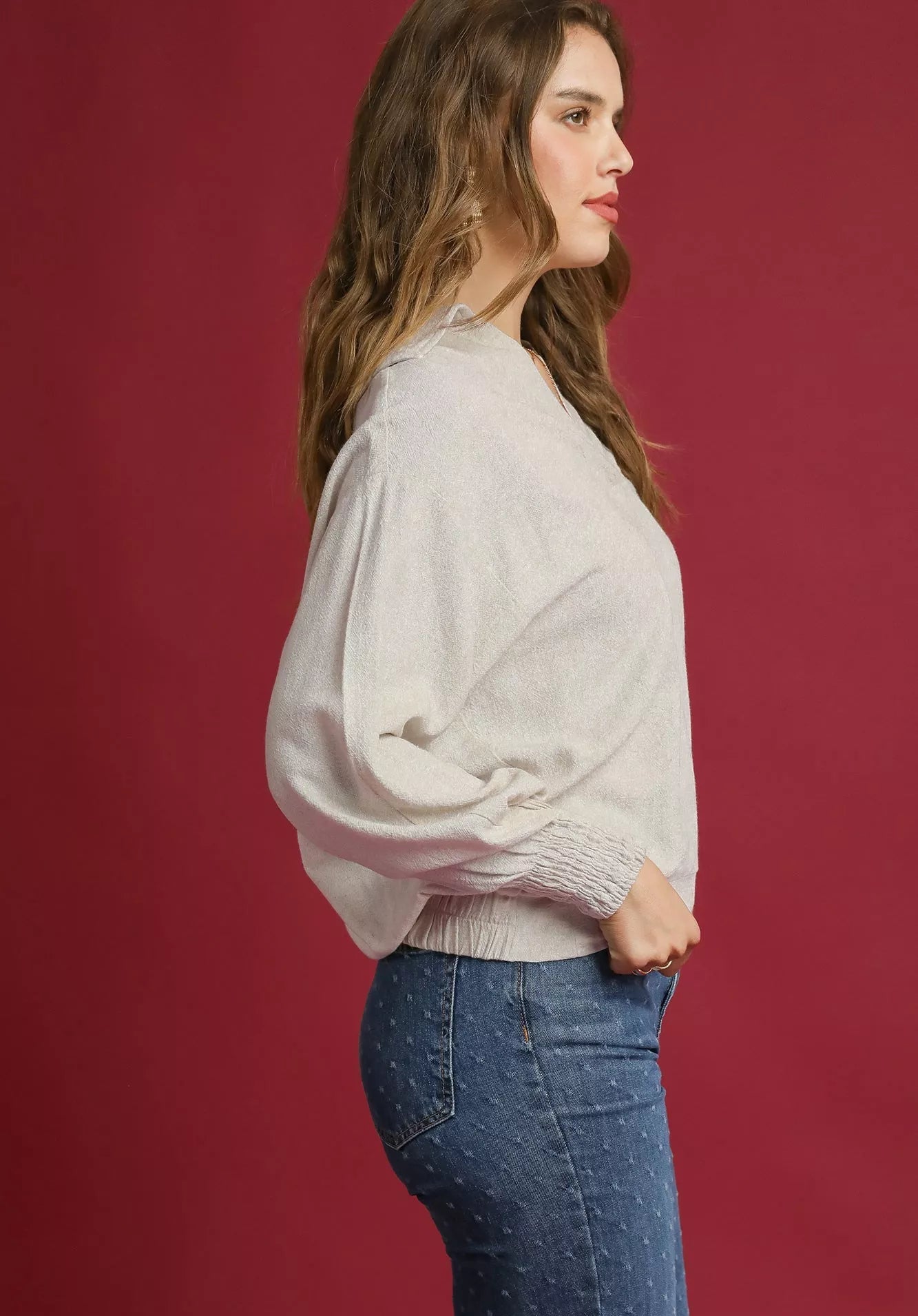 Woman wearing a light-colored sweater and blue jeans against a red background