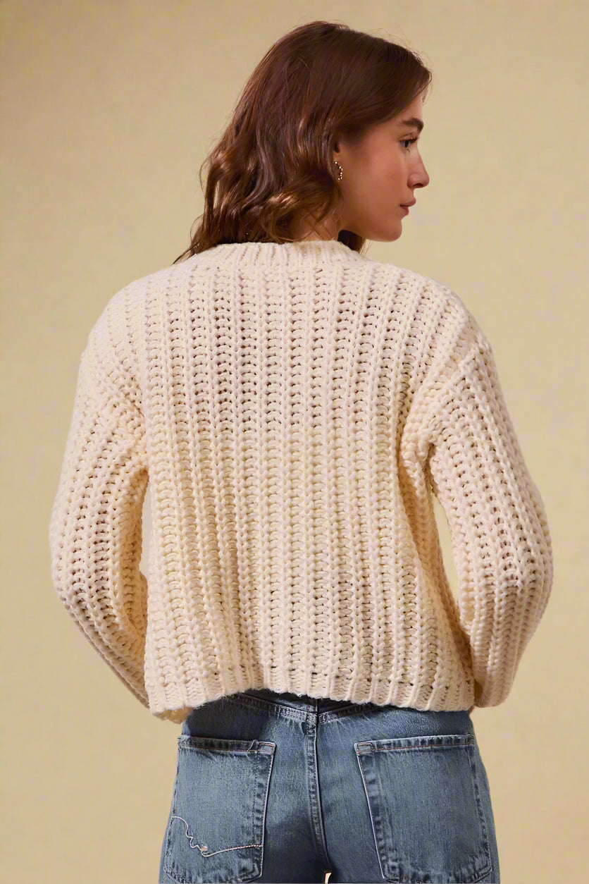 Person wearing a beige knitted sweater and blue jeans on a beige background