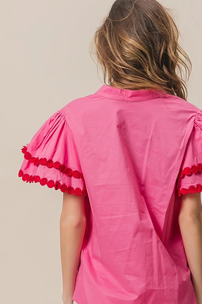 Pink blouse with red pom-pom details on a beige background