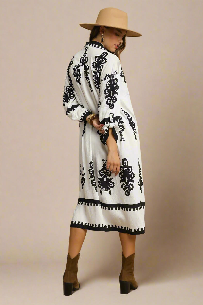 Woman wearing a white dress with black patterns, brown hat, and boots on a beige background