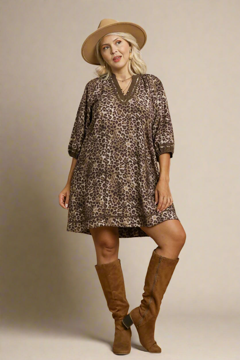 Woman wearing a leopard print dress with a hat and brown boots on a beige background