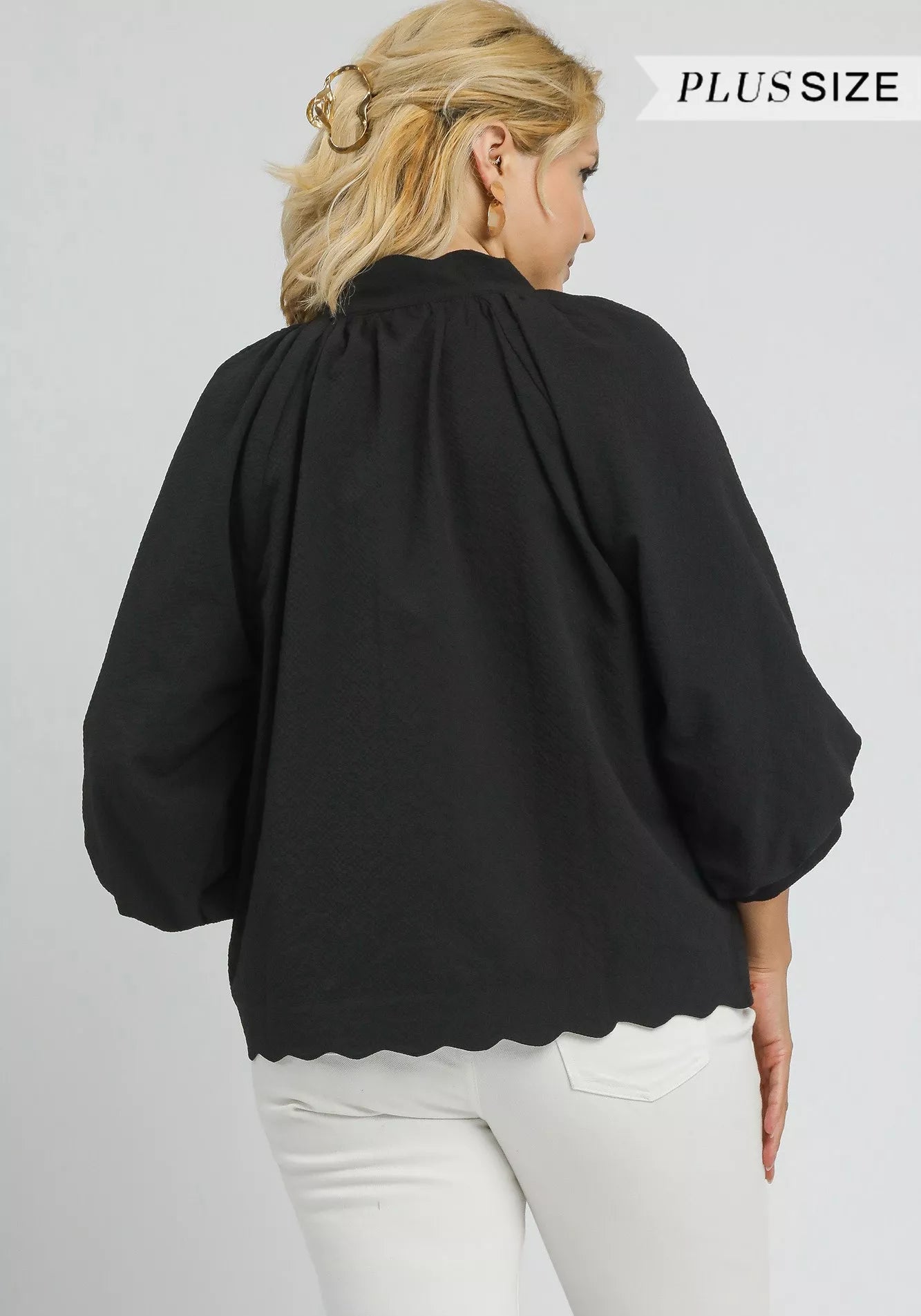 Woman wearing a black blouse with scalloped hem on a gray background