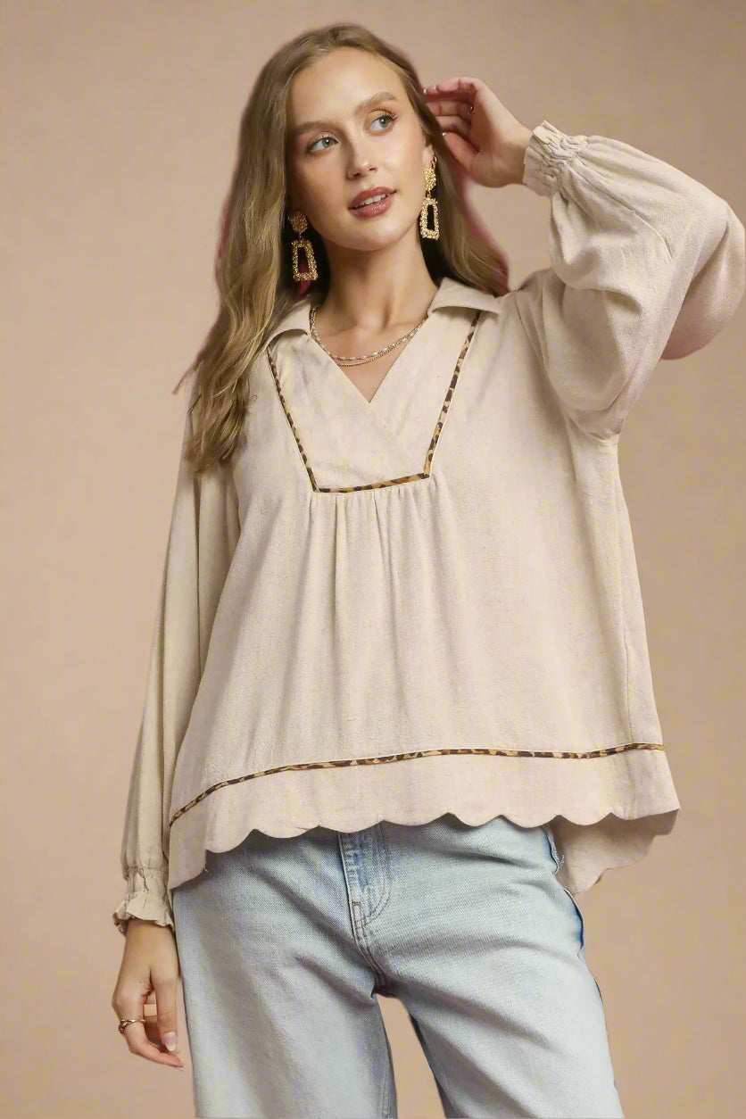 Woman wearing a beige blouse with scalloped edges and light blue jeans against a beige background