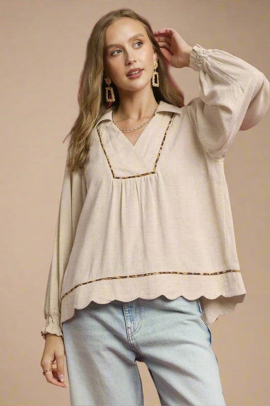 Woman wearing a beige blouse with scalloped edges and light blue jeans against a beige background