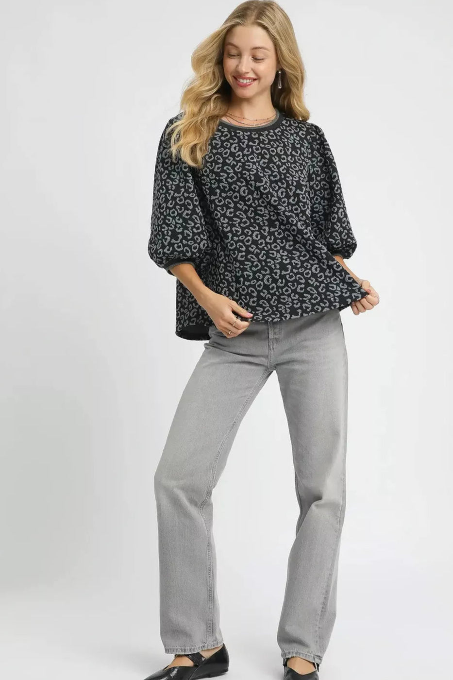 Woman wearing a black floral sweater and gray jeans on a white background