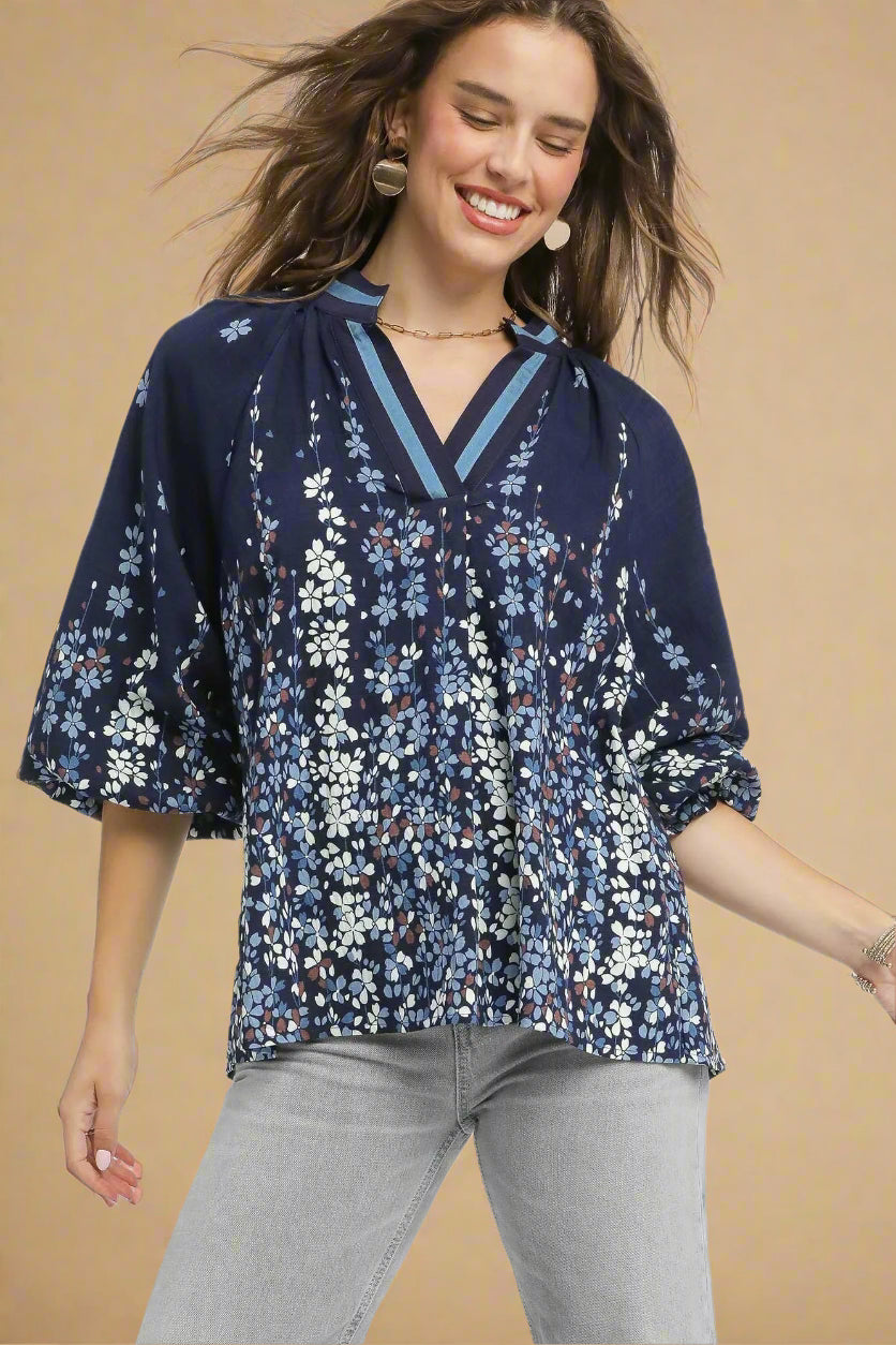 Woman wearing a navy floral blouse with gray pants on a beige background