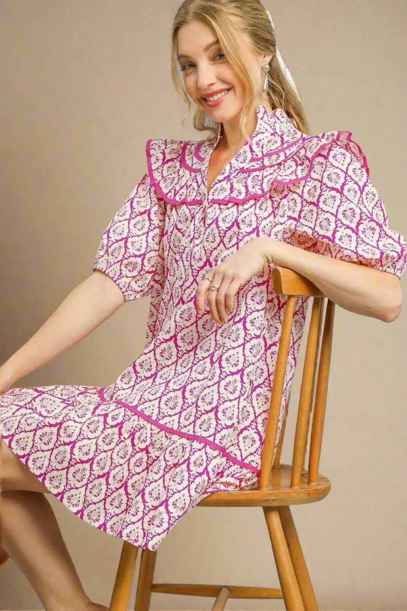 Woman wearing a pink and white patterned dress sitting on a wooden chair against a beige background