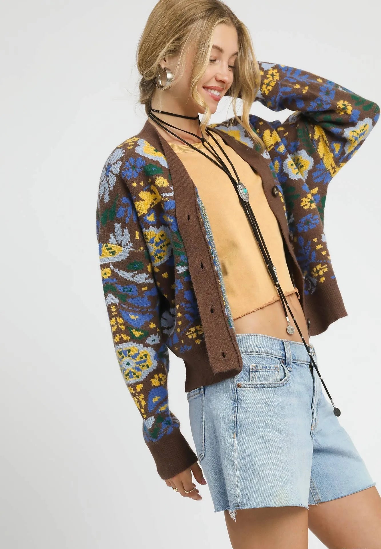 Woman wearing a colorful floral-patterned jacket over a brown cardigan on a white background