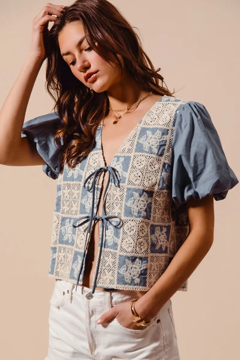 Woman wearing a patterned top with blue sleeves against a beige background