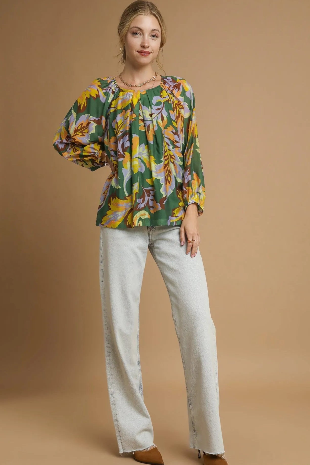 Woman wearing a colorful floral blouse and light-colored pants on a beige background