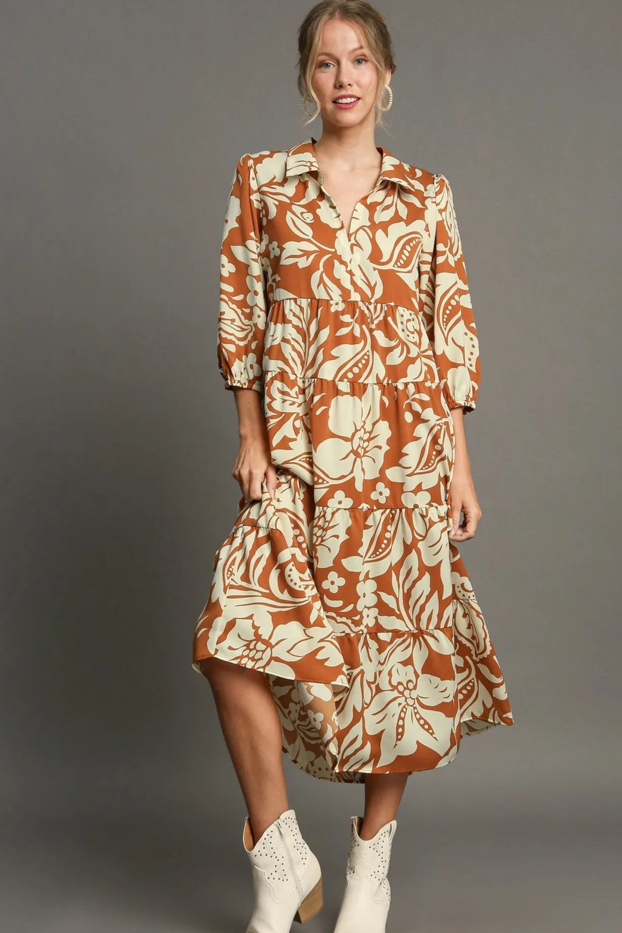 Woman wearing a rust-colored floral dress with white boots on a gray background
