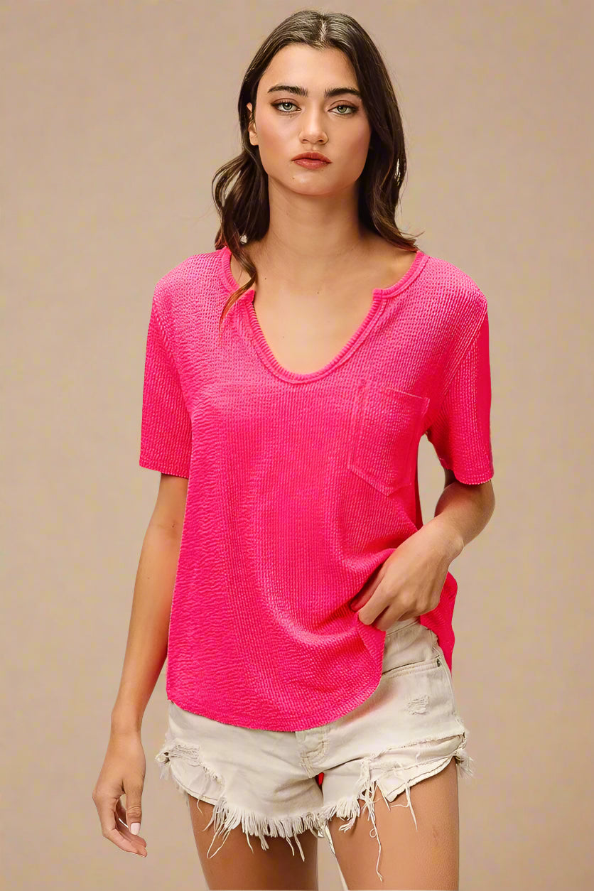 Woman wearing a bright pink textured top and light-colored shorts on a beige background