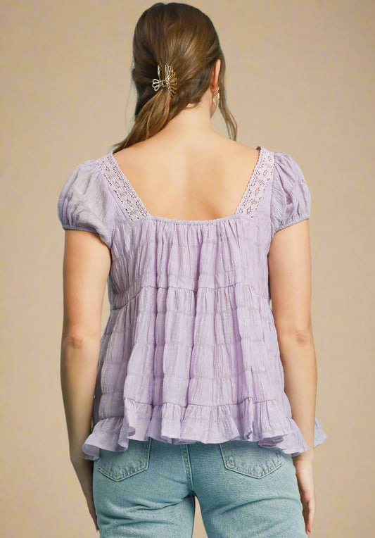 Woman wearing a lavender blouse with ruffled layers on a beige background