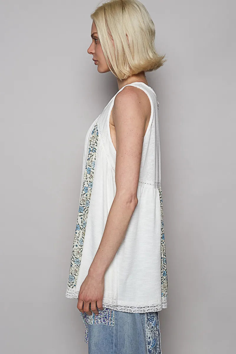 Woman wearing a white sleeveless top with floral patterns on a gray background