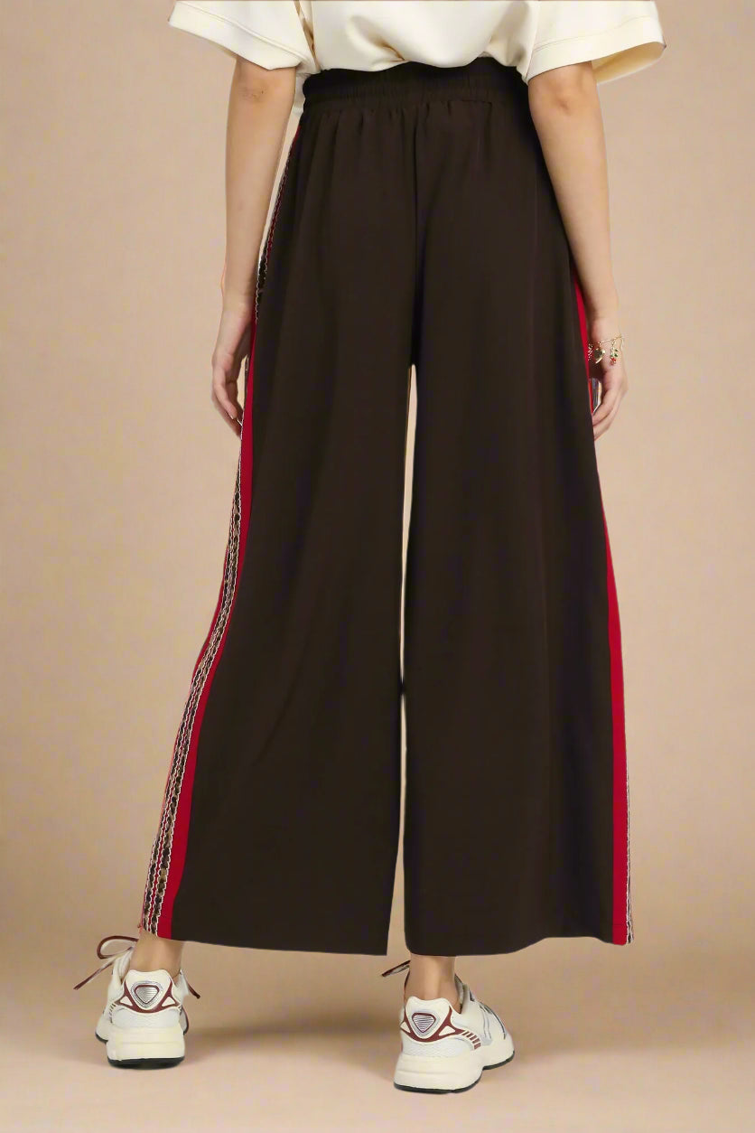 Brown wide-leg pants with red and white side stripes on a plain background