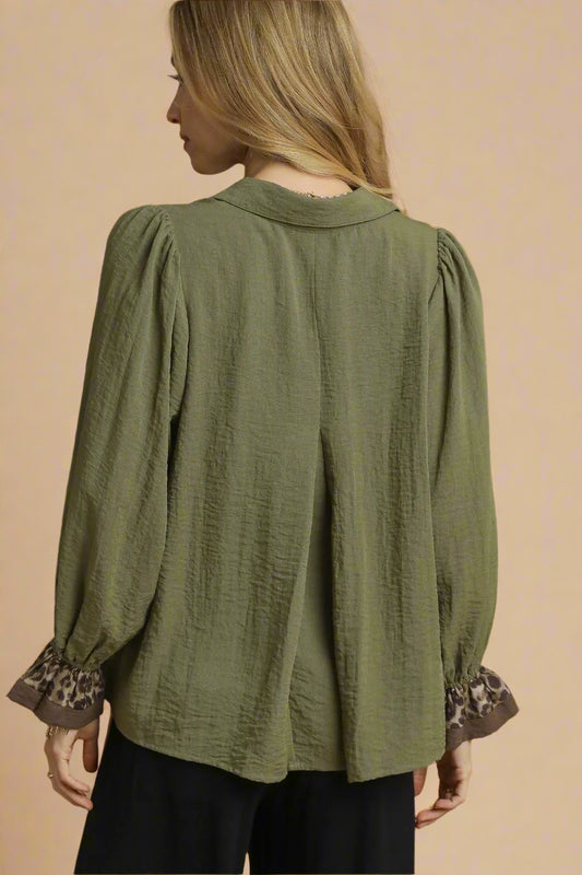 Woman wearing an olive green blouse with leopard print cuffs on a beige background