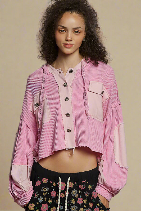 Woman wearing a pink textured jacket with floral pants against a beige background