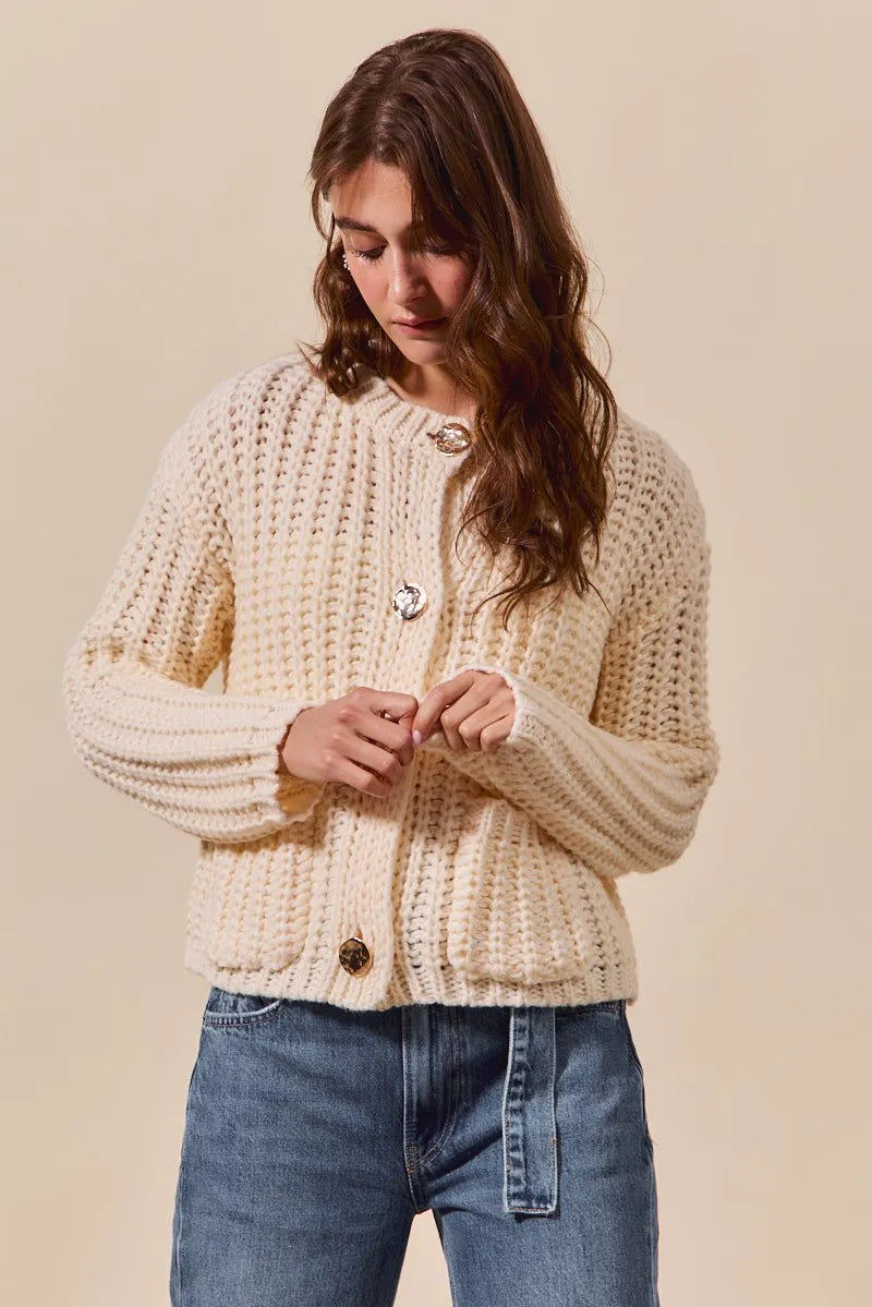 Woman wearing a beige knitted cardigan and blue jeans against a beige background