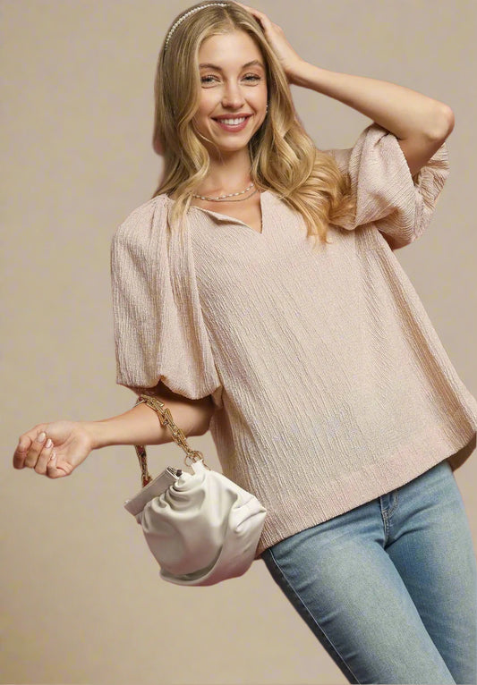 Woman wearing a beige sweater and blue jeans, holding a white handbag against a red background