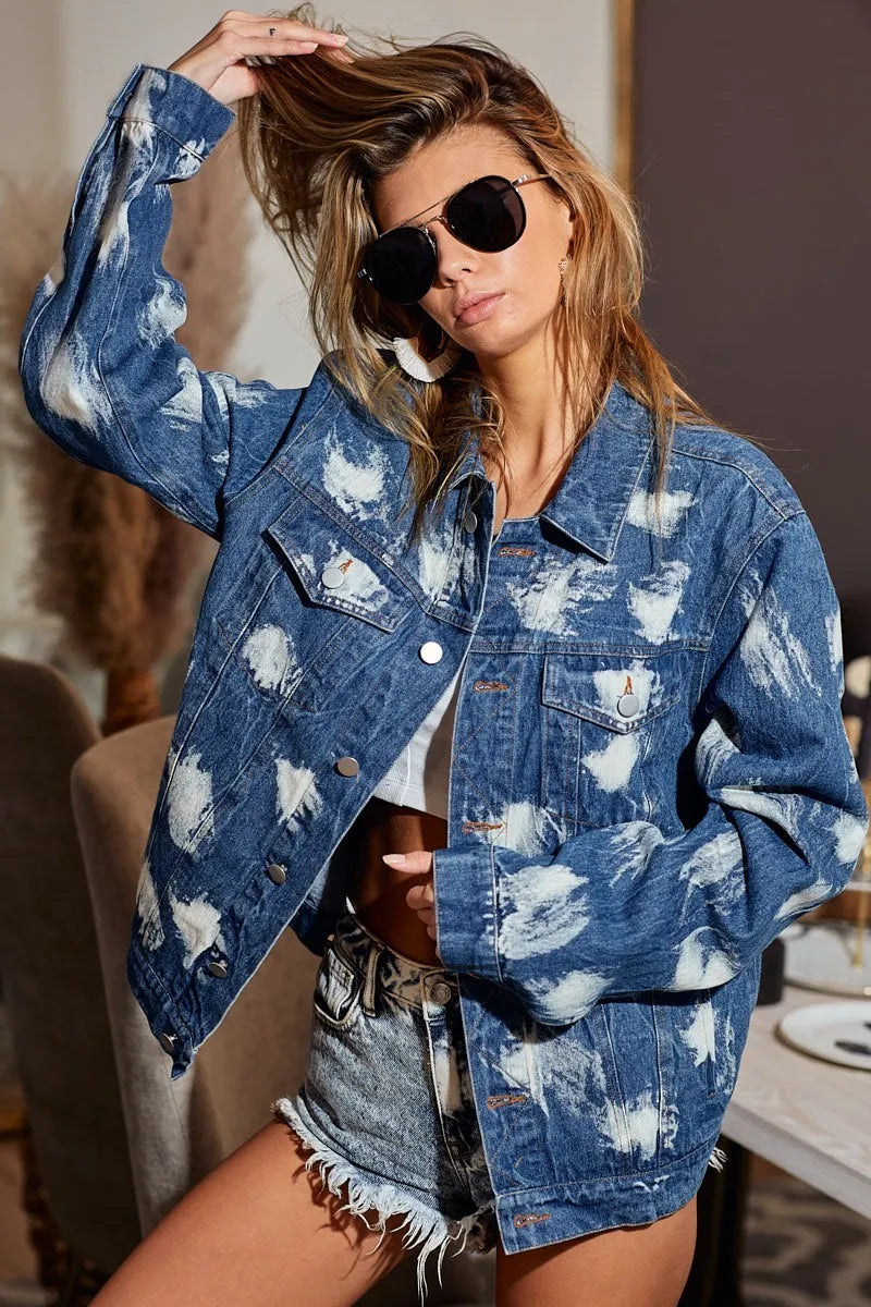 Woman wearing a blue denim jacket with white patterns and denim shorts indoors.