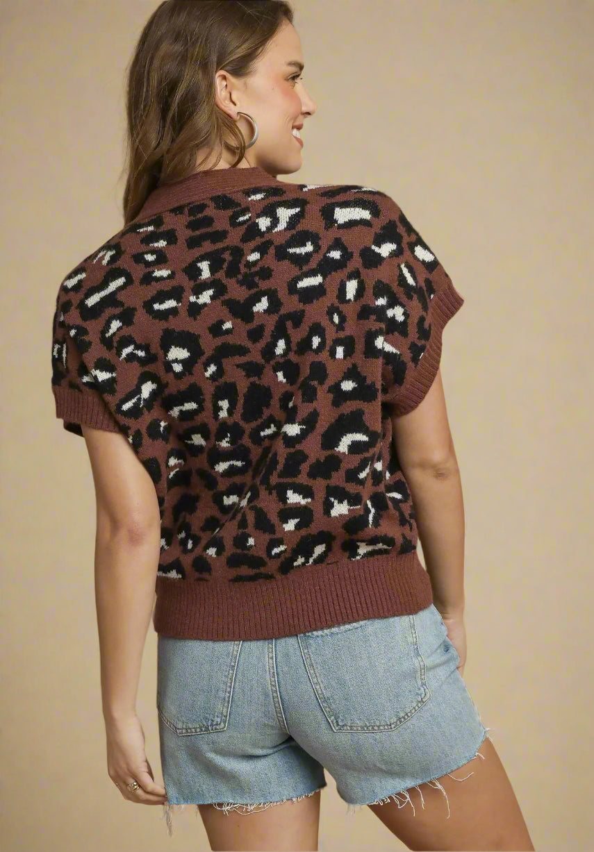 Woman wearing a brown leopard print sweater and denim shorts on a beige background