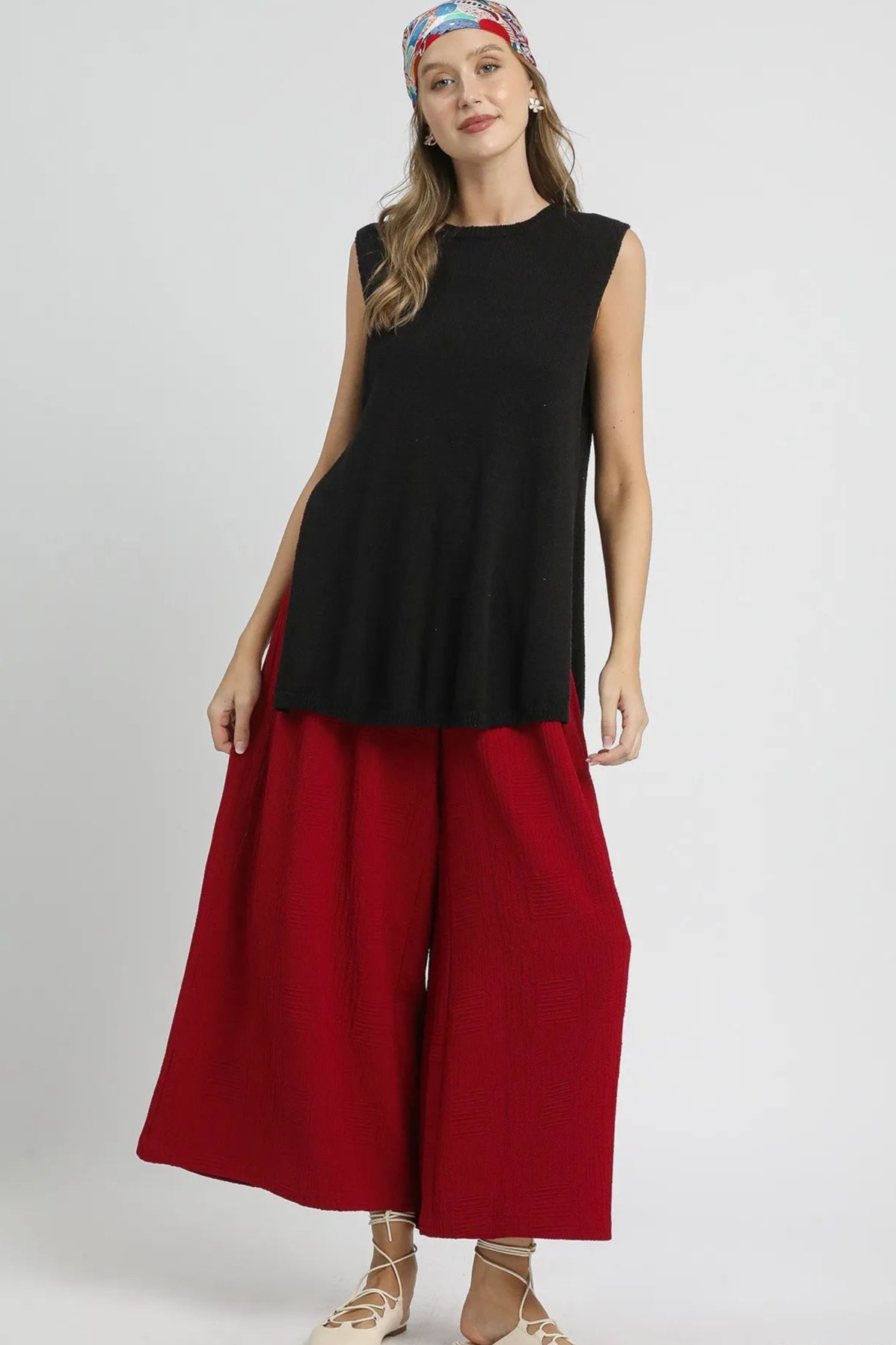 Woman wearing a black sleeveless top and red wide-leg pants on a white background